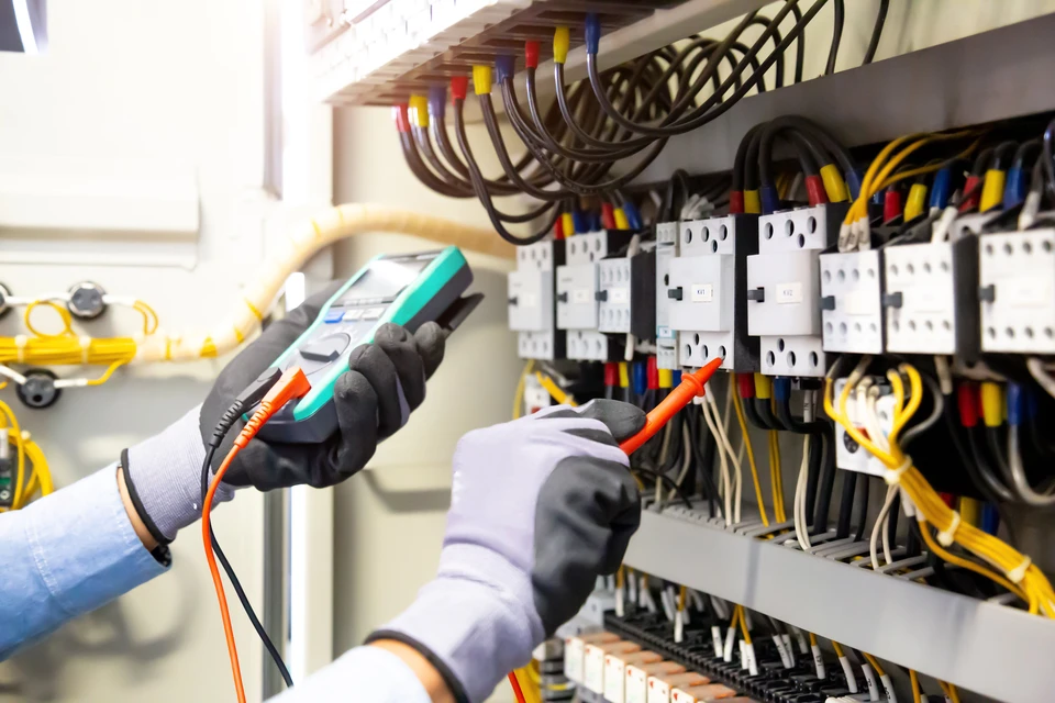 Électricien professionnel en combinaison travaillant sur un tableau électrique industriel, testant les circuits avec un multimètre