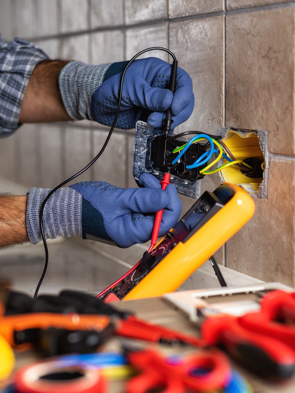 Électricien professionnel en combinaison et gants de protection bleus travaillant sur installation électrique murale