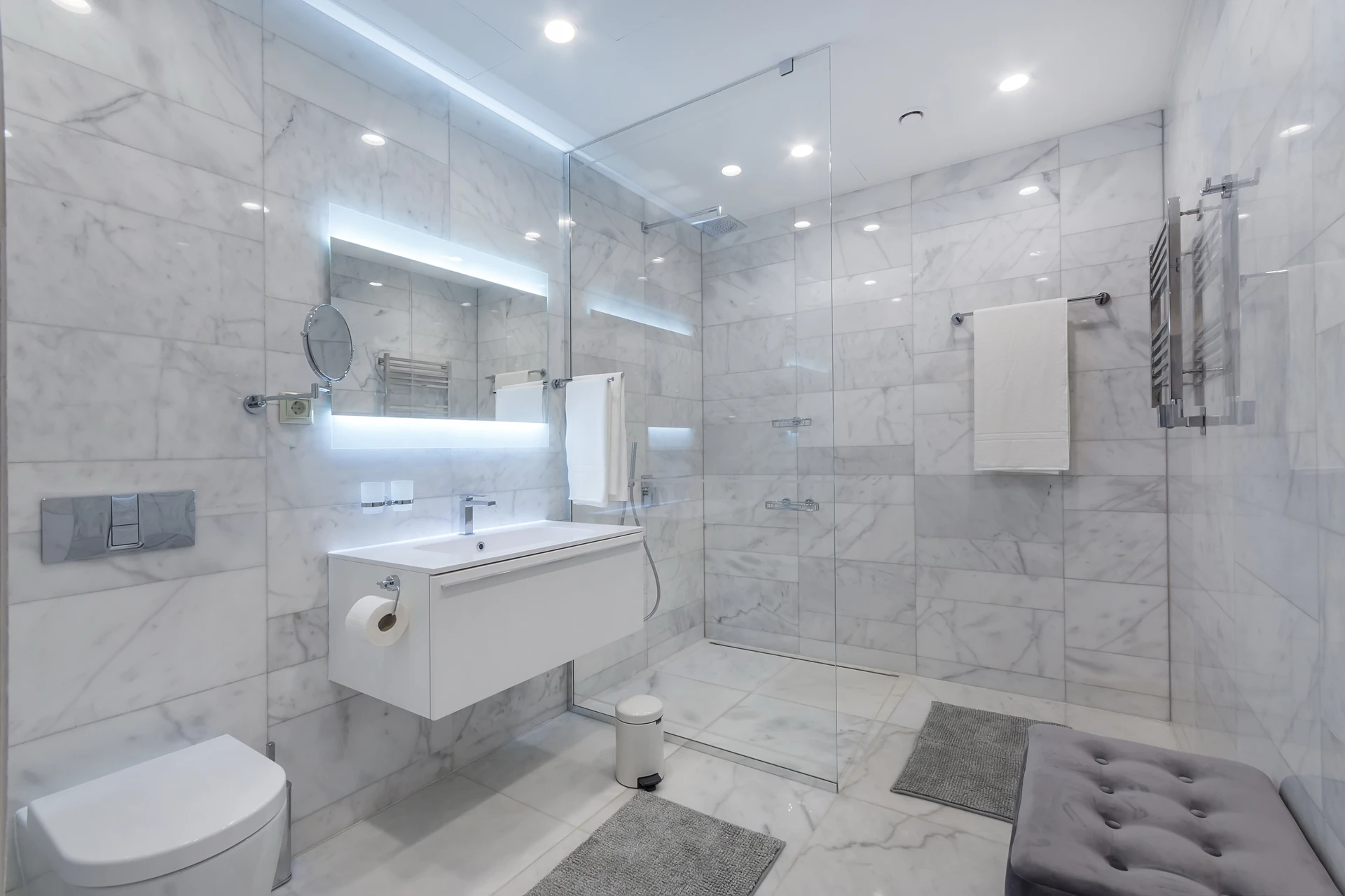 Salle de bain moderne luxueuse avec douche à l'italienne vitrée, carrelage mural en marbre blanc veiné gris, meuble vasque suspendu blanc laqué, miroir rétroéclairé LED