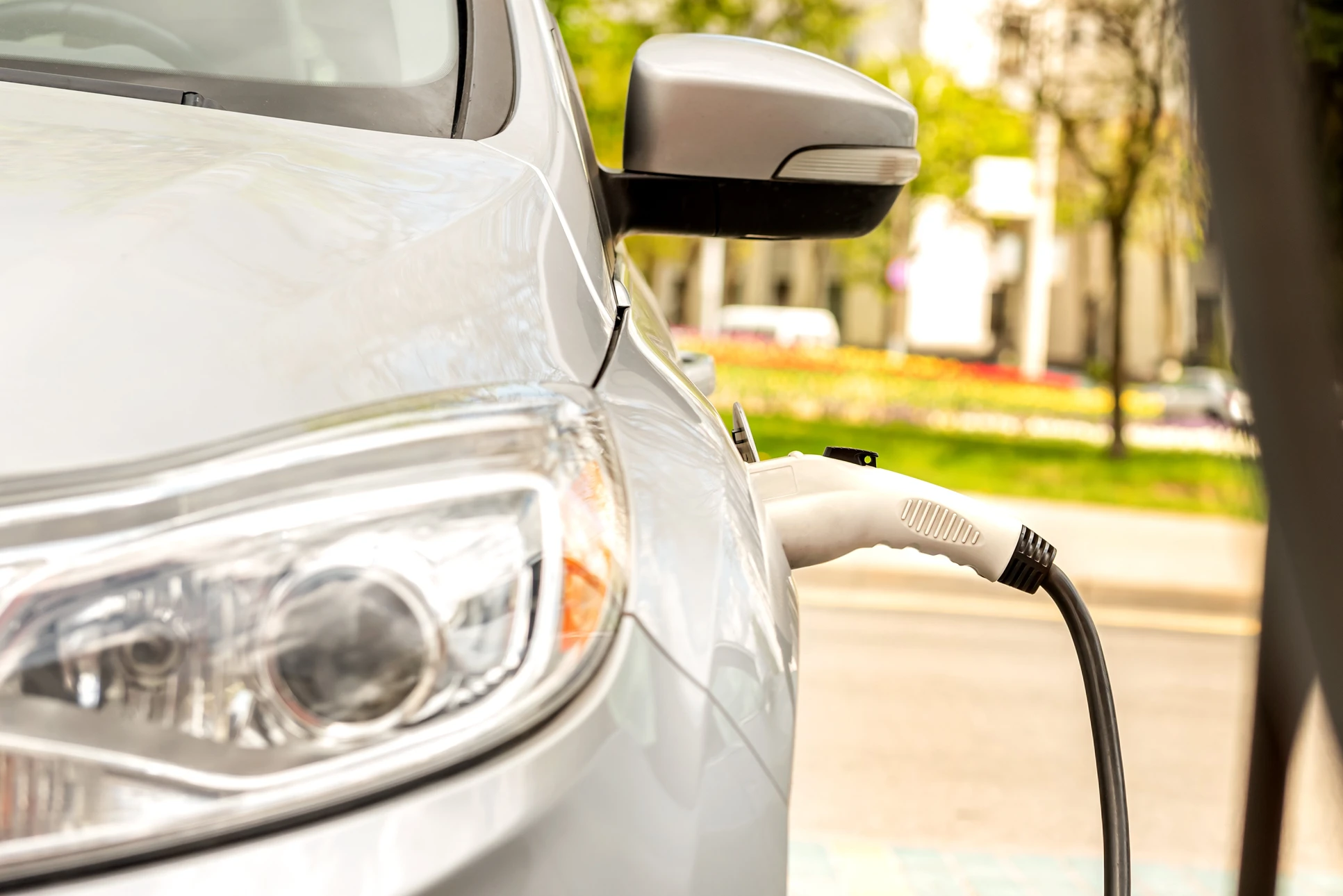 Voiture électrique blanche en cours de recharge sur une borne publique dans un environnement urbain arboré