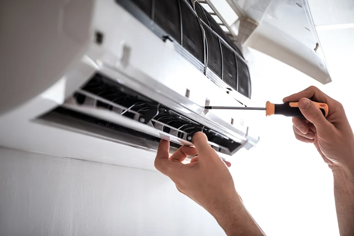 Extérieur résidentiel avec unité extérieure de climatisation fixée sur clôture en bois alternant lattes brunes et beiges