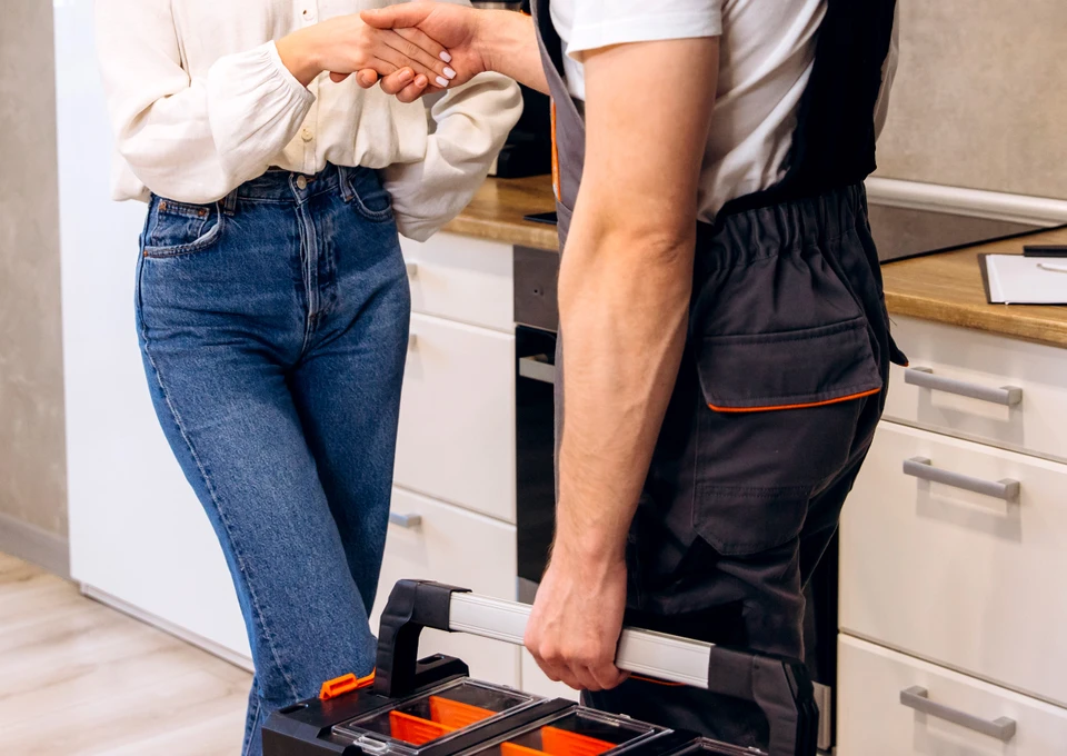 Photographie d'une équipe de trois professionnels (électricien, plombier et chauffagiste identifiables par leurs outils respectifs) travaillant ensemble sur un chantier de rénovation intérieure. Les trois hommes en tenue professionnelle et équipement de sécurité (gilets de travail) sont visibles en train de collaborer autour d'une installation technique (canalisation, coffret électrique visible en arrière-plan, ou équipement de chauffage). L'atmosphère doit montrer la cohésion, l'entraide et la concentration professionnelle. Cadrage serré sur l'équipe en action, chantier professionnel en arrière-plan. Lumière naturelle ou artificielle professionnelle. Photo réaliste de qualité professionnelle.